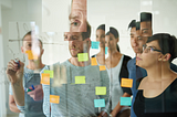 A team standing at a whiteboard brainstorming. Each member of the team is distorted so that their faces look misaligned.