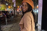 author on busy city street at night time, wearing orange hat