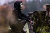 Boy with Guy Fawkes mask sitting down, looking to the distance