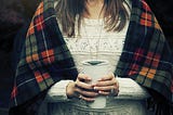 woman in a blanket holding a mug.