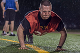 Army sergeant doing “one more rep” of push-ups outside in the rain, and with visible strain on his face.
