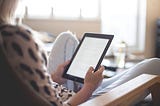 Woman sat in an armchair at home holding a tablet