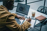 https://www.pexels.com/photo/crop-black-businessman-writing-on-paper-near-laptop-in-cafeteria-5648032/