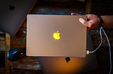 Apple 14-inch MacBook Pro with magsafe charger plugged in, orange light shinning on Apple logo