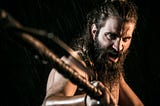 Hard, bearded man with a threatening pose wielding a stick