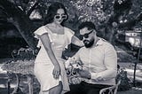 A fashionable-looking man and a woman are sitting outdoors at a table