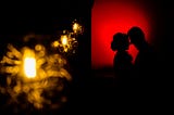 A silhoutte photo of a couple with red lit background as their foreheads are pressed against one another.