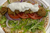 Three yellow pea falafels in a warm whole grain pita with hummus, lettuce, tomato, and onion, topped with tzatziki sauce.