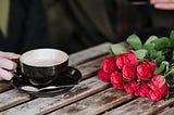 Faceless couple with coffee and rose bouquet in cafeteria