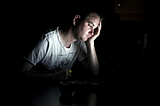A young man in a T-shirt with his hand on his head, looking down and depressed.