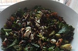 A salad with dark green spinach leaves, chopped roasted carrot and broccoli, toasted pecans and goats cheese with balsamic