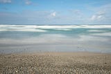 Photograph of a beach, ocean and sky in which the waves have been blurred by a long exposure.