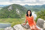 Lady in an orange dress with a lake and green hill in the background