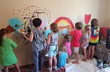 Eight young children painting a “happy mural” on an interior wall.