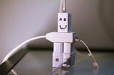Three white plugs plugged into a white extension cord with a face drawn on so it looks like a robot