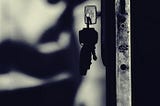 dark door with keys hanging from the lock a shadowy figure in the back