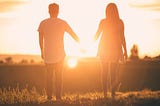 a couple walking in a field into the sunset holding hands