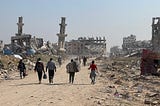 Several individuals walk with backs to camera through a war-torn area