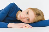 A woman with a somber expression, lying on her side on a white surface