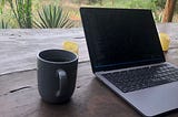 A MacBook pro with a cup of coffee sits on a wooden desk