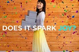 Marie Kondo smiling at the camera while carrying boxes. Caption reads: Does it spark joy?