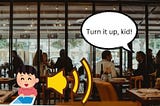 Stylized image of a cartoon child with an ipad sitting at a table in a real looking restaurant. There is a yellow volume symbol in the middle and a speech bubble coming from another table with the words “Turn it up, kid!”