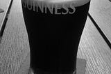 A black and white photo of a pint of Guinness half-drunk, on a table with a beer mat.