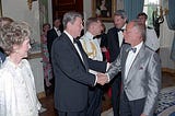 President Reagan shaking Roy Cohn’s hand, Nancy Reagan looking on, at a fancy dress event in the White House.