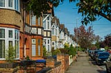 Residential street in West London with terraced houses, parked cars and tree-lined pavement on a clear day