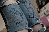 picture of a student’s legs in ripped jeans with Sharpie drawings on them.