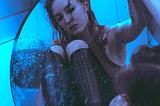 A girl looking in a mirror in the bath tub and she is very sad.