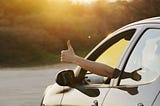 Person sticking thumbs up outside of car window