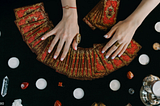 An image of tarot cards fanned out over a table and the reader’s hands hovering over them.