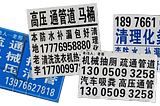 Four advertising stickers pasted on a wall. All of them features skewed Chinese Gothics with numerals resembling the typeface Univers.