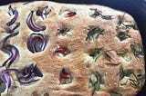 A homebaked focaccia bread loaf with red onions, chilis, rosemary, garlic, and sea salt.