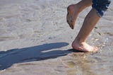 A photo of someone running on the beach, we only see the legs and feet