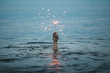 Hand coming out of a dark body of water holding up a light sparkler