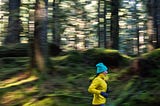 Female in yellow jacket running through moss-covered forest