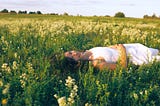 Woman in a white sundress laying in a field of flowers.