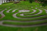 A grassy labyrinth shown in a partially-loaded photo that is clear on the top and blurry at the bottom.