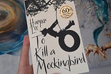 A hand holding a book called To Kill a Mockingbird