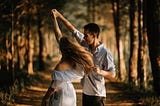 A girl and a boy expressing love as they joyfully dance together amidst nature’s beauty.