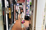 A lady standing in the middle of an alley, turning back to face the camera with a smile on her face.