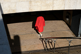 A photo of the back of a woman at the bottom of a set of stairs leading into a metro station. She’s wearing bright red overcoat and white Converse shoes with bare legs. The shadow from the entrance of the station makes it look like the woman has no head.