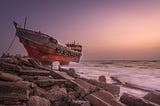 A man sits looking at a wrecked ship on the rocks