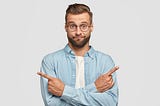 Hesitant and clueless man crosses hands over chest, indicates with index fingers in different sides or directions, can’t make choice between two different career choices available to him