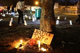 A sign reading “Justice for Tyre” leans against a tree with several lit candles in the frame.