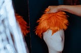 A hand grabs an orange wig from a dummy head.