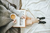 A woman reading a book with a cup of coffee.