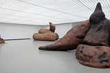 A large white room in an art gallery with three enormous sculptures in the shape of turds